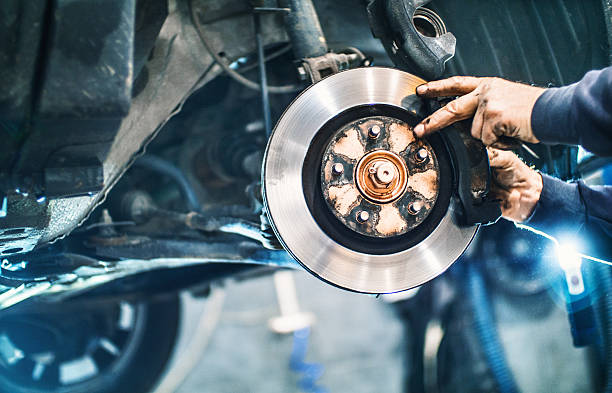 Car braking system repair. Closeup of unrecognizable male mechanical replacing worn out brake pads on a vehicle. The wheel has been removed and the car is lifted up on a jack. Visible braking disc. Side view. brake disc photos stock pictures, royalty-free photos & images