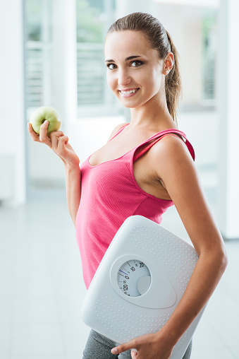 Smiling teenage girl holding a scale and a fresh apple, healthy eating, fitness and weight loss concept