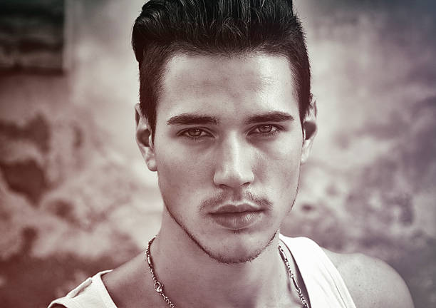 Extreme close-up portrait of a young man wearing make-up, ear jewelry, and stubble – a modern view on self-expression and queer youth culture.