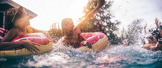 teen amigos mergulhar em uma piscina com coloridas inflatables - floating on water fotos - fotografias e filmes do acervo