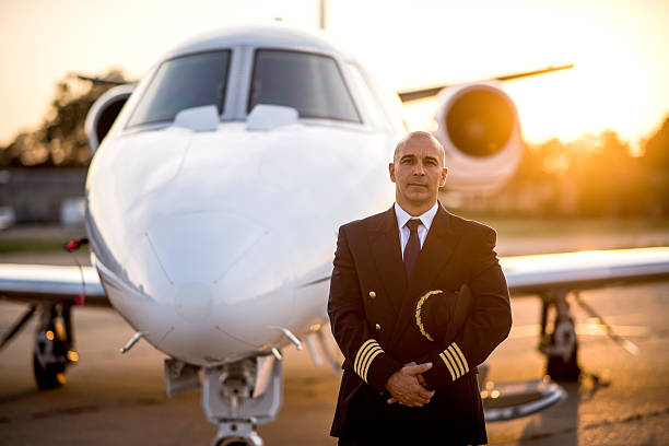 Captain of private jet aeroplane Portrait of a pilot in uniform holding his cap in front of the private jet aeroplane. Sunrise is in the background. piloting photos stock pictures, royalty-free photos & images