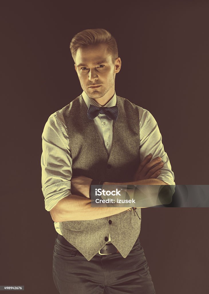 Handsome elegant man wearing bow tie and tweed vest Fashionable elegant man wearing tweed vest, shirt and bow tie, looking at camera. Dark tone, black background. Blond Hair Stock Photo