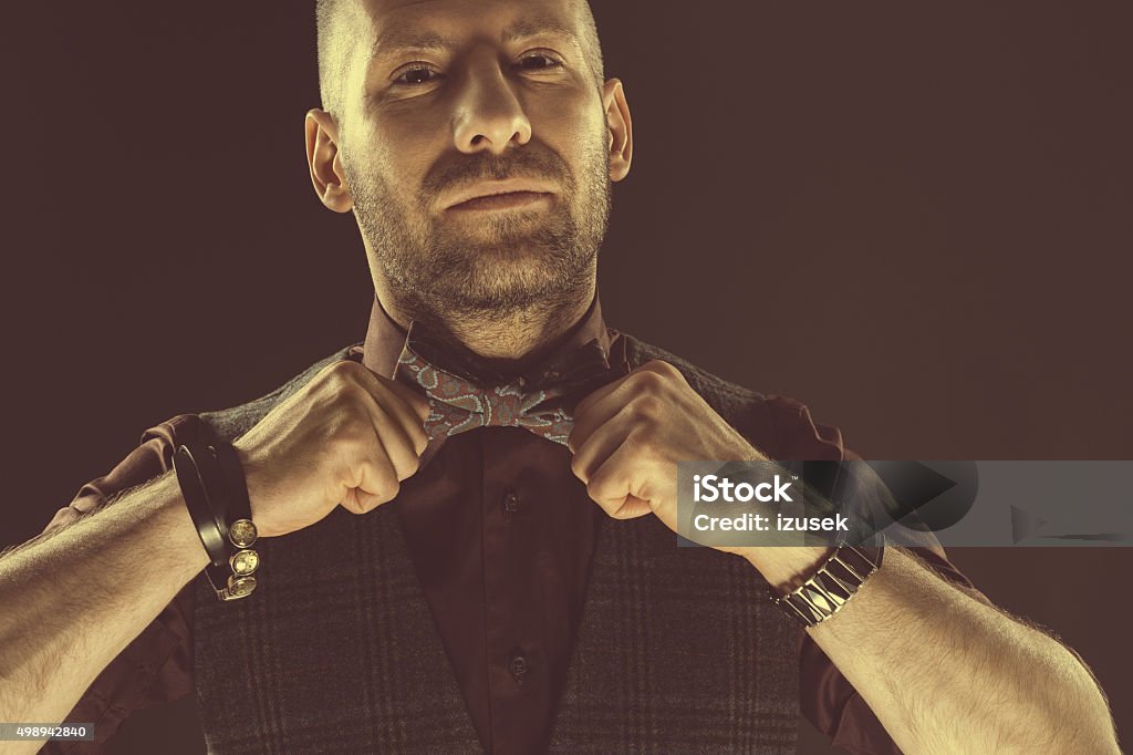 Handsome elegant man wearing bow tie Handsome elegant man wearing tweed vest, shirt and bow tie, looking at camera. Dark tone, black background. 2015 Stock Photo
