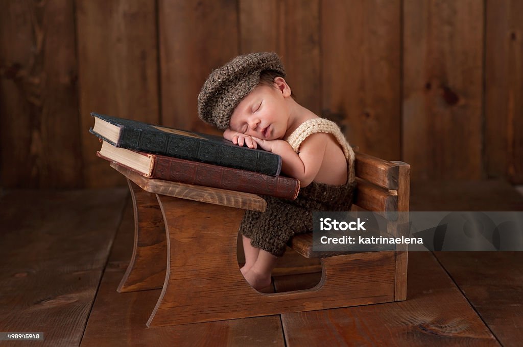 Newborn Baby Boy Sleeping at his School Desk Three week old newborn baby boy wearing crocheted cap, shorts and suspenders. He is sitting at a tiny school desk and sleeping on a stack of vintage books. Babies Only Stock Photo