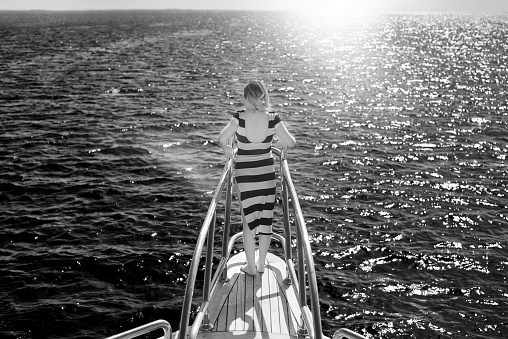 black and white shot of young woman on boat, feeling the wind and the feeling of freedom.sunlight in the sea.