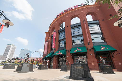 St Louis, USA - September 2, 2015: Team shop from outside with bronze statues  baseball greats at Saint Louis Ballpark Village  home to St. Louis Cardinals in downtown St. Louis, city hih-rise and Gateway Arch in background,  Missouri, USA.