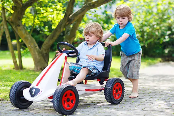 Photo of Two happy twin boys driving toy car