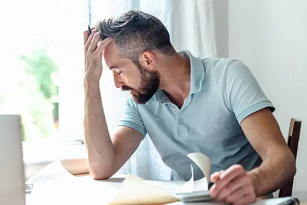 stressed bearded creative men holding head in head at desk in home office