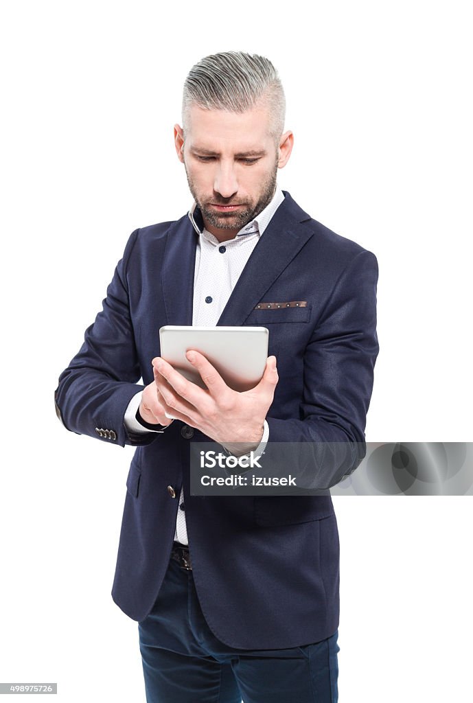 Bearded grey hair businessman using a digital tablet Portrait of elegant bearded grey hair businessman standing against white background and using a digital tablet. Studio shot, one person.  2015 Stock Photo