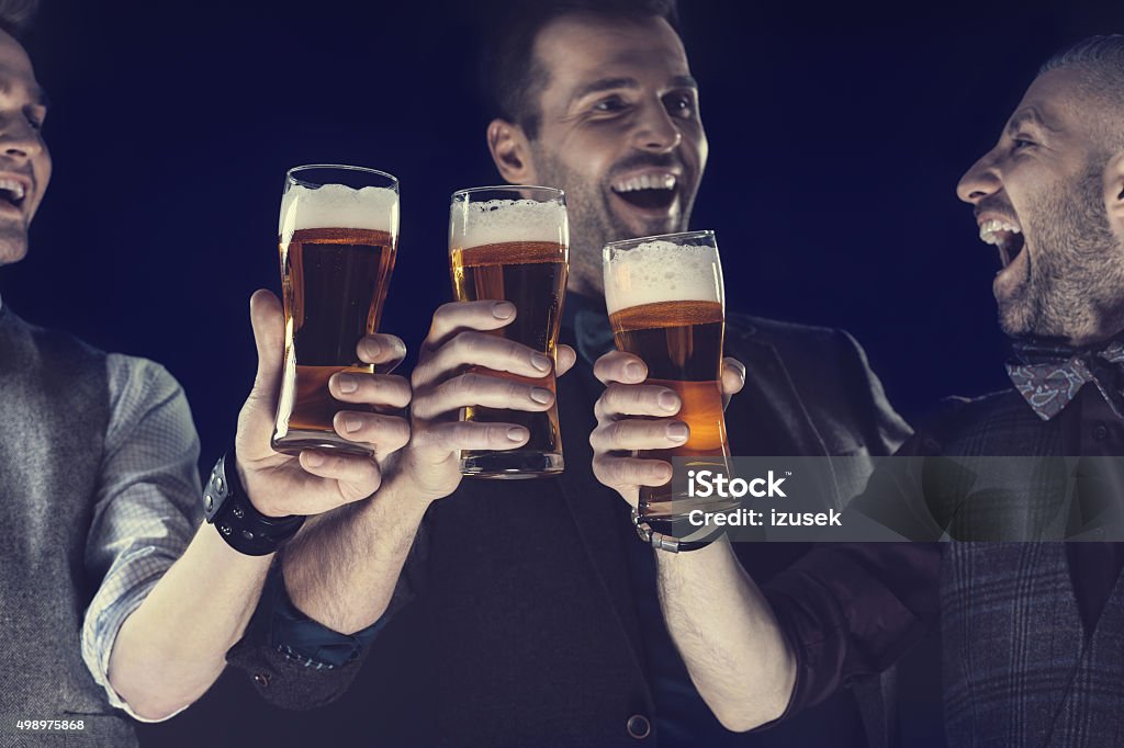 Happy elegant men toasting with beer Happy friends toasting with beer, raising hands, laughing. Close up of hands and beer glasses. Beer - Alcohol Stock Photo