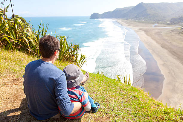 family in new zealand back view of family sitting at the top of lion rock at piha beach, new zealand north island new zealand stock pictures, royalty-free photos & images