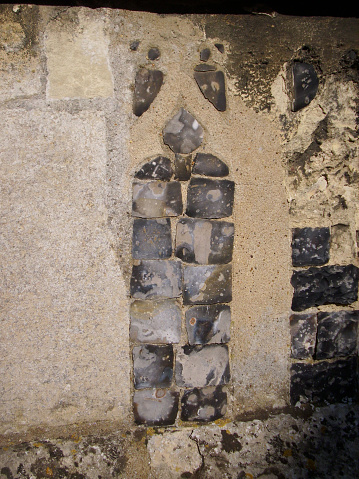 Pieces of ornamental flint cut, knapped and set into the stone of a church wall in an ornamental pattern.