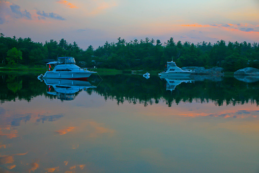 Two cruisers are anchored in Chimney Bay, Georgian Bay, Ontario, Canada the colored clouds are reflecting in the water from the sunrise.