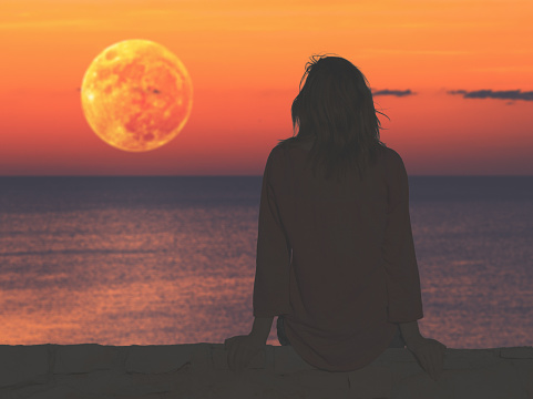 Girl watching the ocean/sea horizon with a Moonrise.