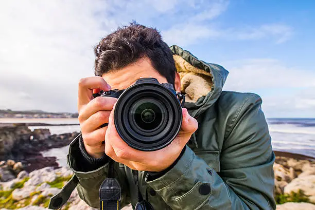 A young man using a DSLR camera at the sea