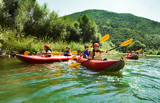 A group of mature rafters wearing safety gear paddle a raft amidst the changing leaves of a serene river landscape.