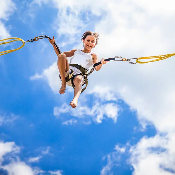Little girl jumping at trampoline - flights against the blue sky 