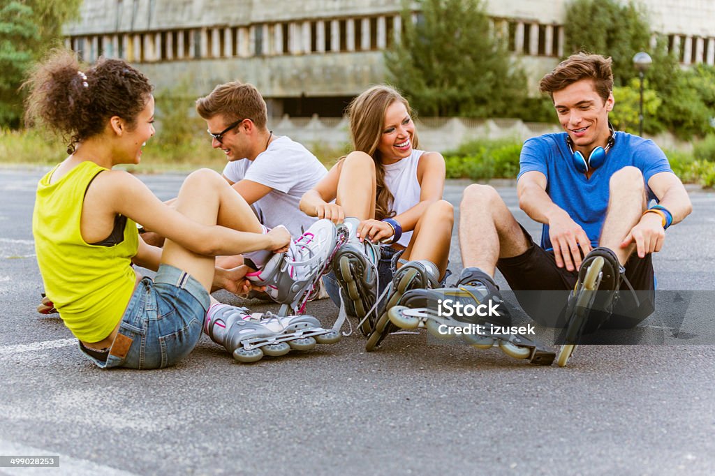Young people on rollerblades Four friends sitting on tarmac and tying rollerblades. 20-24 Years Stock Photo