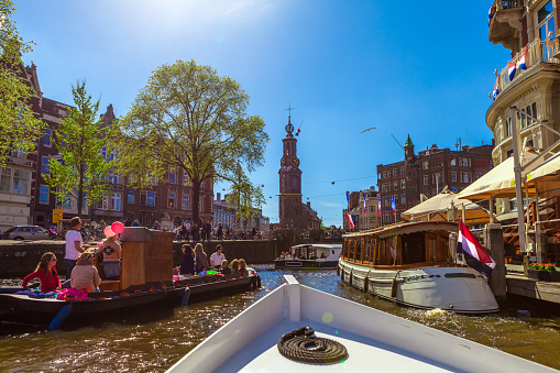 Typical canal in Amsterdam. Visible are restaurants, sightseeing tourism canal boats, typical dutch houses, bridges and Tower in Centrum. Amsterdam, Netherlands.