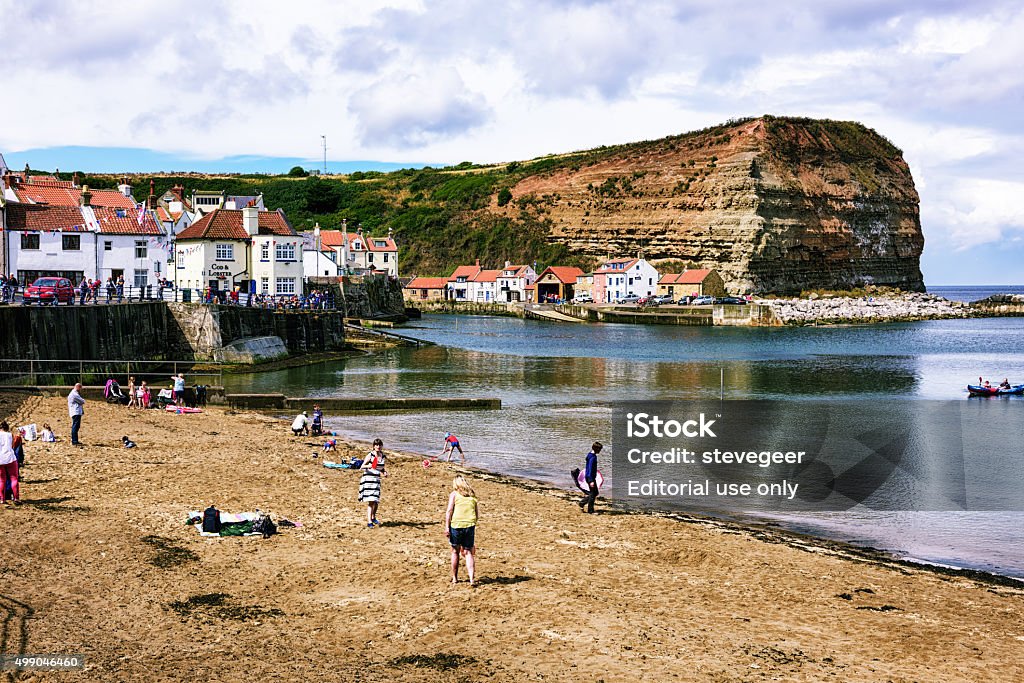 Harbour and Sandy Shore at Staithes, North Yorkshire Staithes, England - August 10, 2015: The harbour and sandy shore at Staithes in North Yorkshire, England. Many people on beach and waterfront. Yorkshire - England Stock Photo