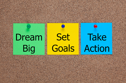 Three blanks post-it notes on corkboard with words Dream Big, Set Goals, Take Action.