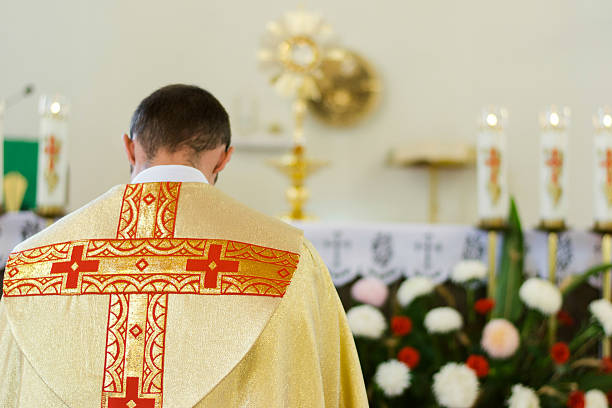 Priest of the Catholic Church in yellow clothes bows The priest of the Catholic Church in yellow clothes bows to Crucifixion in front of flowers and candles liturgy photos stock pictures, royalty-free photos & images