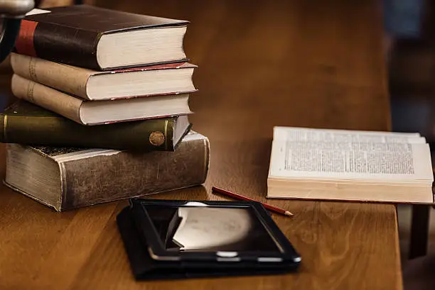 Photo of Digital tablet and a pile of books on wooden table