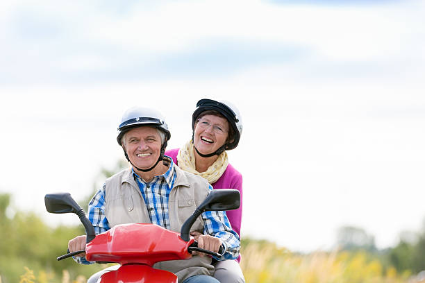 feliz pareja senior con ciclomotor en un día soleado - senior adult action couple motor scooter fotografías e imágenes de stock