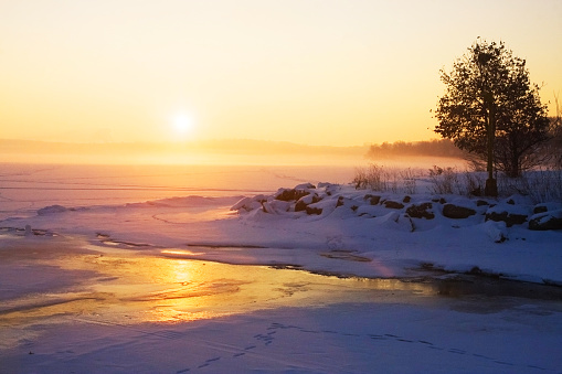 Beautiful winter landscape with misty winter sunrise over a frozen lake
