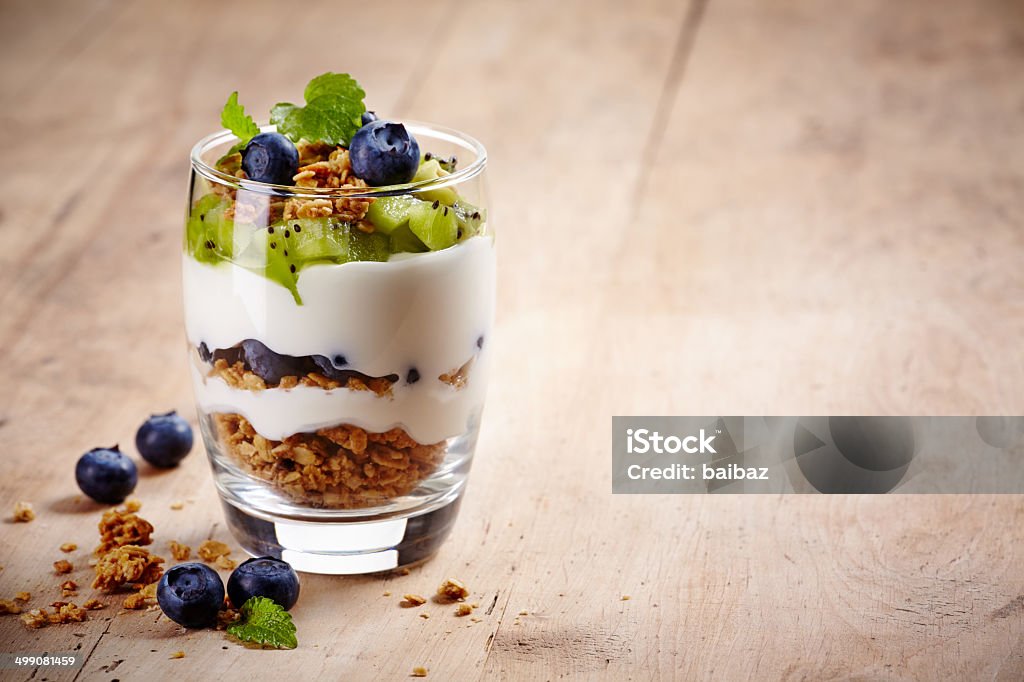 Layered cream dessert Healthy layered dessert with cream, muesli, kiwi and blueberries on wooden background with space for text Yogurt Stock Photo