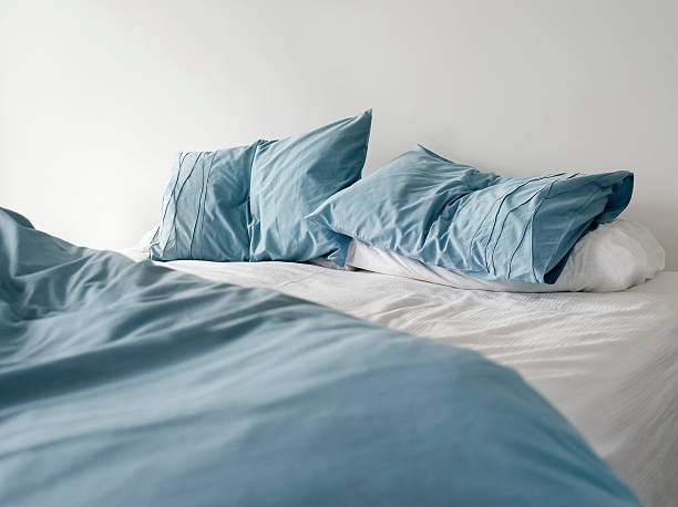 unmade bed with crumpled blue linens stock photo