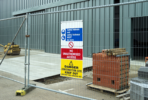 A construction site with a warning sign attached to a metal fence.
