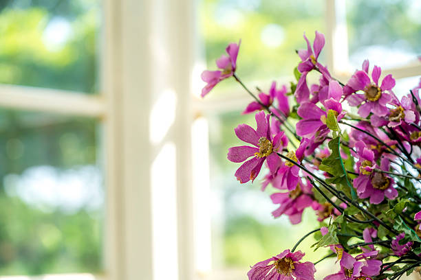 Artificial flowerpot near the glass window and have green tree on a background.