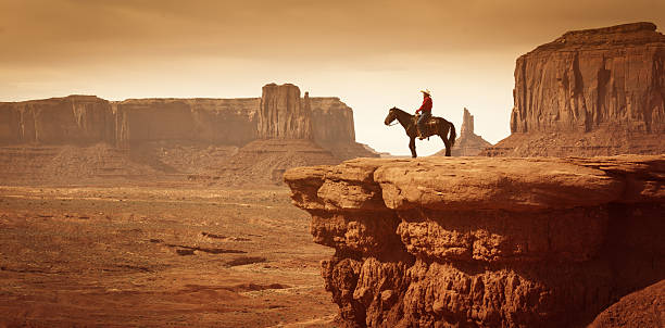 American Southwest Cowboy on Horse Subject: A native American Indian cowboy riding a horse in a desert landscape with plateaus in the distance. monument valley stock pictures, royalty-free photos & images