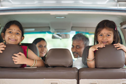 Happy Indian family sitting in car smiling, ready to vacation.  Asian parents and children.