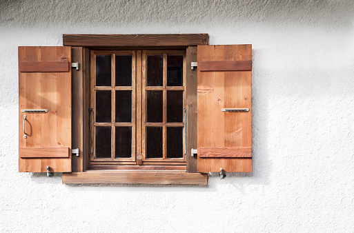 Wooden Swiss chalet window against white wall with wooden shutters.