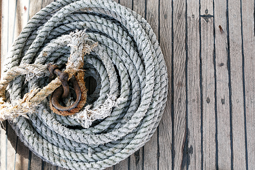 Overhead view of neatly coiled rope on a wooden deck with an attached rusted clasp and copyspace to the right