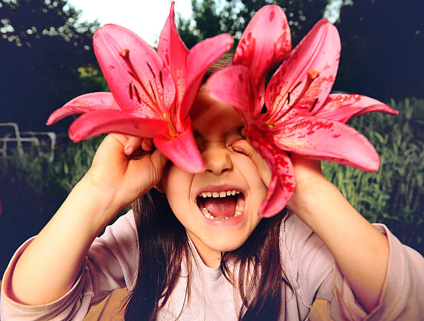 istock Cheerful girl playing with flowers, looking into  camera through  lily 499115075