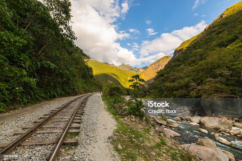 Railway track and Machu Picchu mountains, Peru The railroad track crossing jungle and Urubamba river, connecting Machu Picchu village to hydroelectric station, mostly used for tourism and cargo purpose. Machu Picchu archeological site visible towards the top in the background. Scenic sunset light on the ridge. 2015 Stock Photo