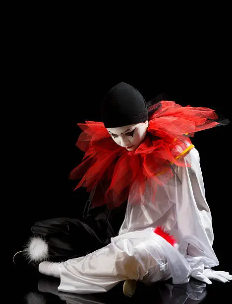 Sad Clown or Pierrot sitting on the black floor