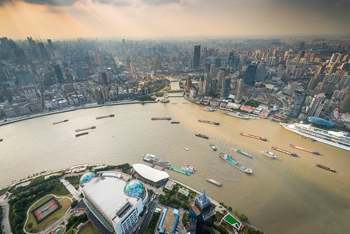 Rays of sunlight filtering through the smog to illuminate the crowded skyscrapers and city blocks of Shanghai, as fleets of barges ferry goods along the Huangpu River in the heart of China's fastest growing city. ProPhoto RGB profile for maximum color fidelity and gamut.