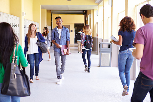 Group Of High School Students Walking Along Hallway Talking