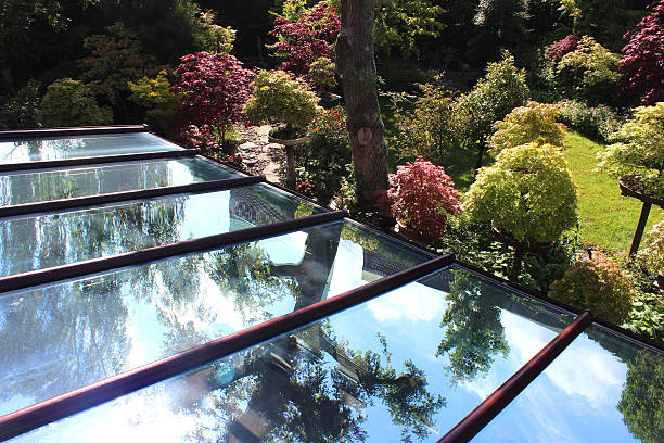 Image of glass conservatory roof panels / panes, reflecting blue sky Photo showing a large glass conservatory roof with brown UPVC dividers, with the individual panels  panes of glass showing reflecting the blue sky and the trees in the surrounding garden. hand tinted stock pictures, royalty-free photos & images