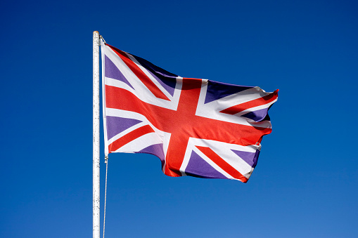 Flag of the United Kingdom waving in the wind against blue sky.