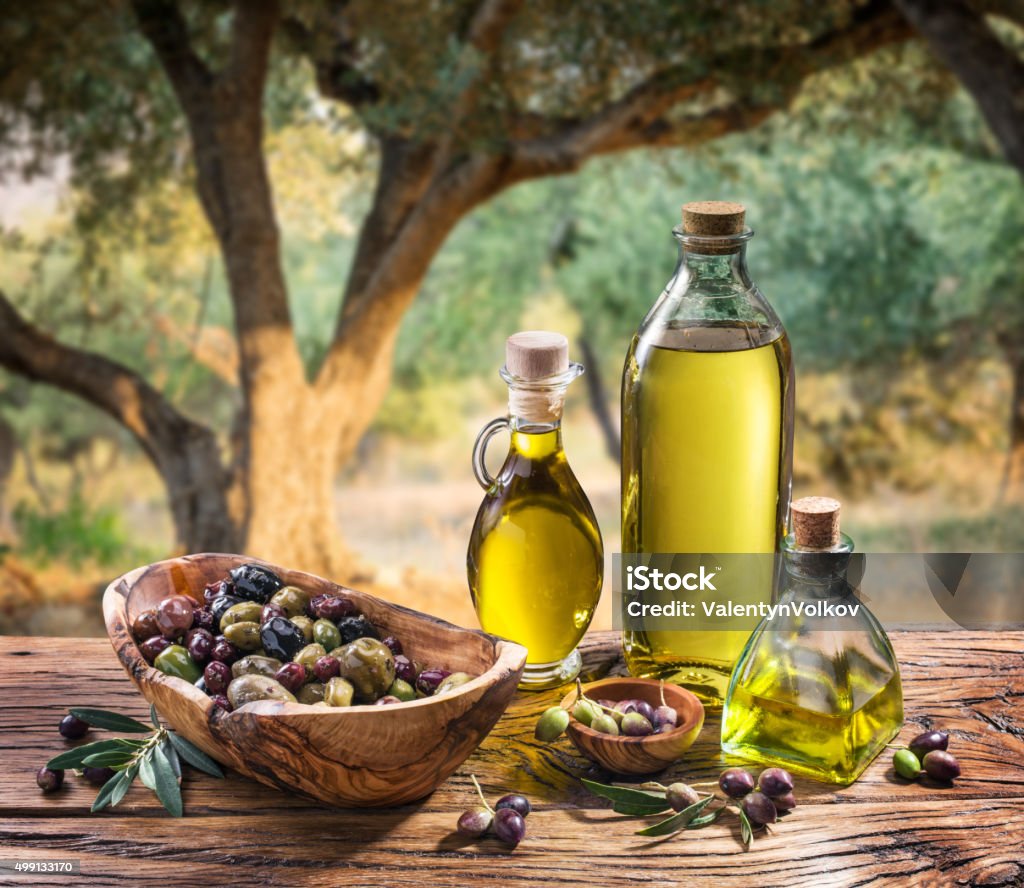 Olives and olive oil on the nature background. Olives and olive oil in a bottle on the background of the evening olive grove. Olive Oil Stock Photo