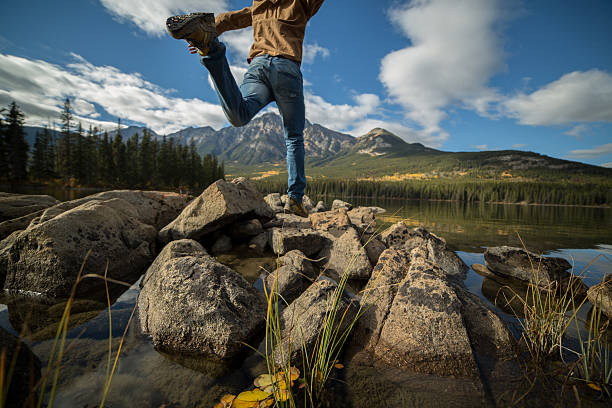 istock Hiker jumps rock to rock in mountain lake.Low angle view. 499133342