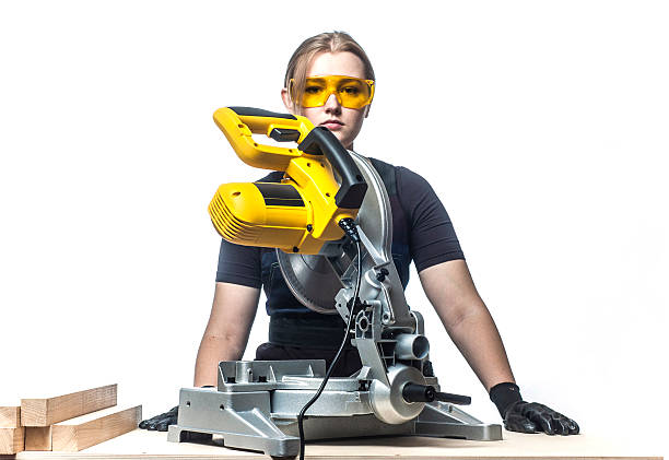 woman with a circular disk saw young beautiful woman in overalls and glasses with disk saw preparing for cutting. Photo on white background. miter saw stock pictures, royalty-free photos & images