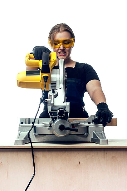 woman with a circular disk saw young beautiful woman in overalls and glasses with disk saw preparing for cutting. Photo on white background. miter saw stock pictures, royalty-free photos & images