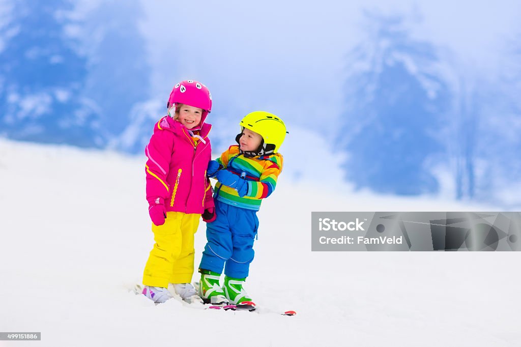 Two children skiing in snowy mountains Children skiing in the mountains. Toddler kids in colorful suit and safety helmet learning to ski. Winter sport for family with young child. Kid ski lesson in alpine school. Snow fun for little skier. Skiing Stock Photo