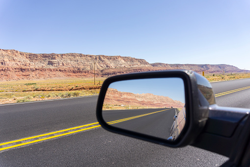 Road and landscape in rear vision mirror through  Arizona long straight roads highly colored landforms